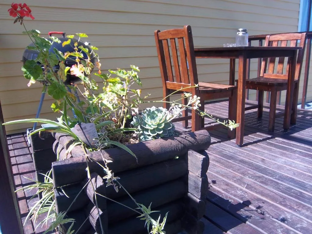Wooden deck with potted flowers and wooden chairs overlooking the garden
