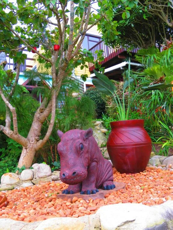 Whimsical purple hippo statue in garden with red pot and native plants