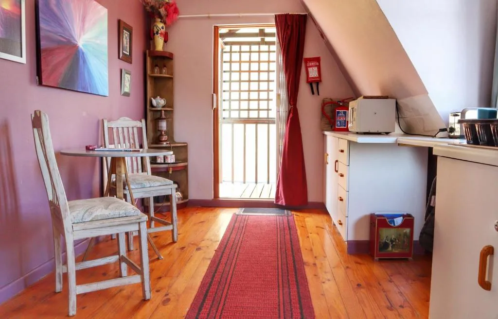 Pink attic room with wooden desk, chairs, and natural light from door