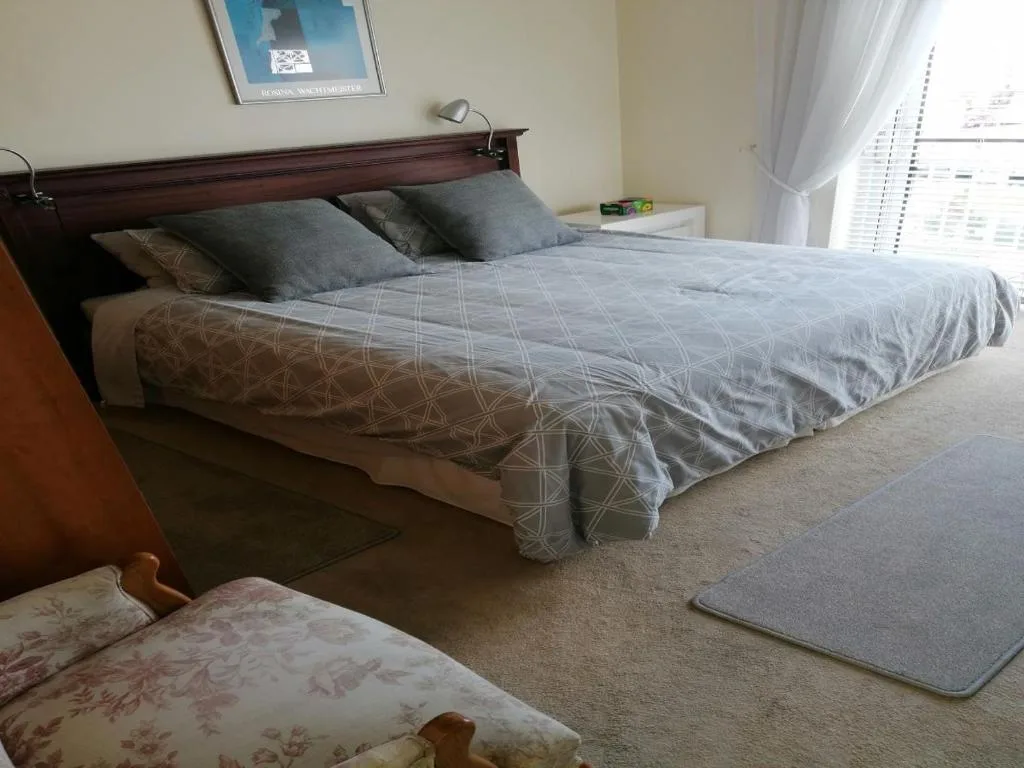 Spacious bedroom with queen bed, grey bedding, dark wood headboard, natural light