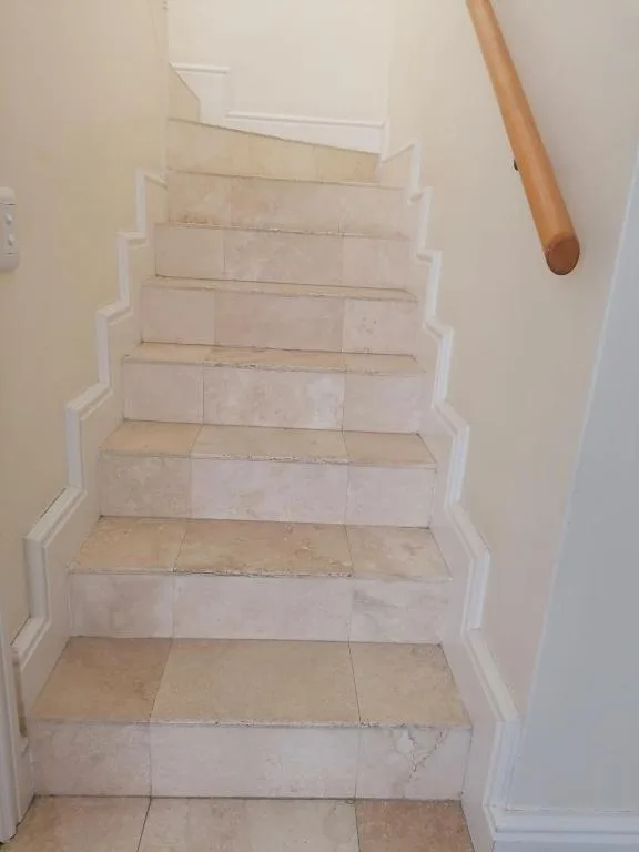 Clean tiled staircase with white painted walls and wooden handrail