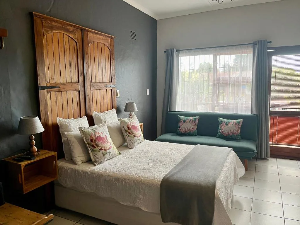 Spacious bedroom with wooden headboard and floral cushions, seating area by window