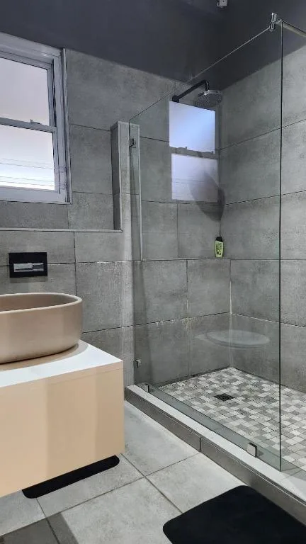 Modern bathroom with grey tile walls, glass shower enclosure, and round vessel sink