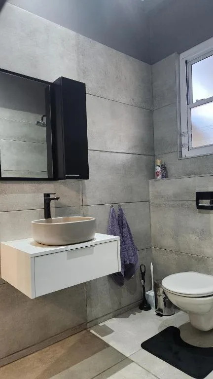Modern bathroom with round vessel sink, black mirror cabinet, and toilet