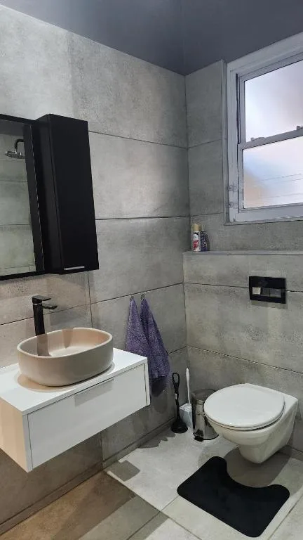 Modern bathroom with round cream sink, black mirror, toilet, and gray tile walls