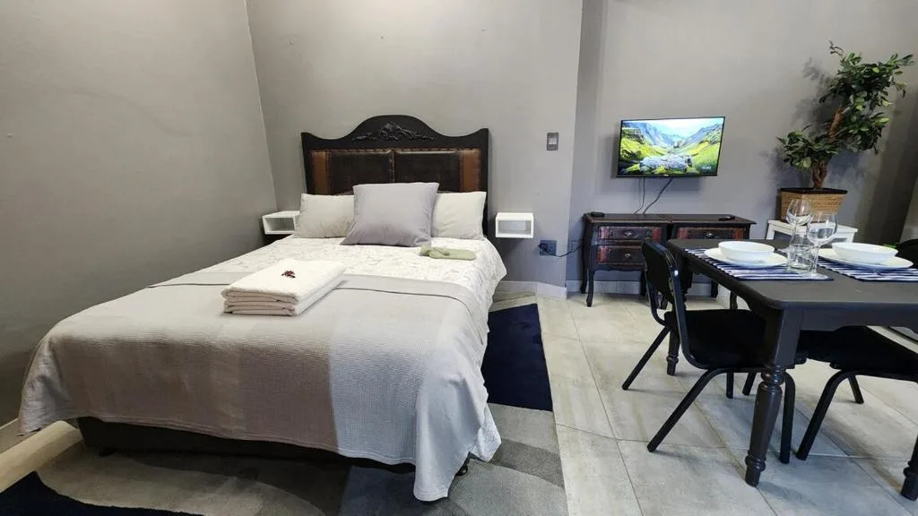 Modern bedroom with queen bed, TV, and work desk area in studio apartment