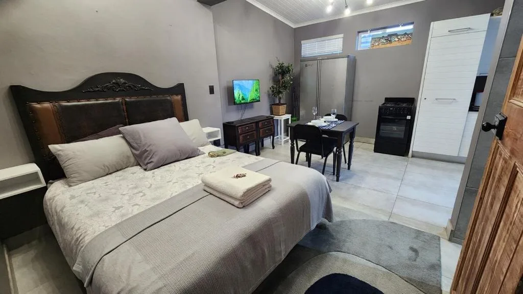 Modern bedroom with black ornate bed, white linens, and en-suite kitchen area