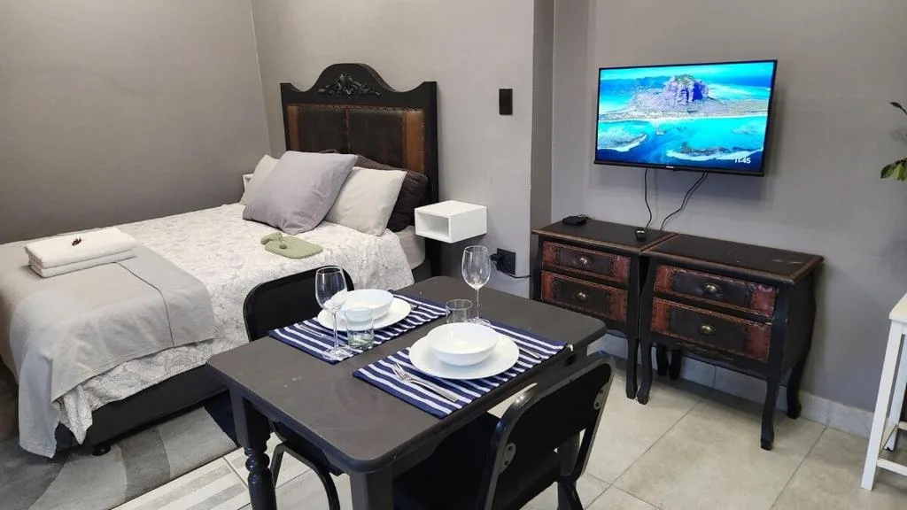 Studio bedroom with bed, dining table, and wall-mounted television display