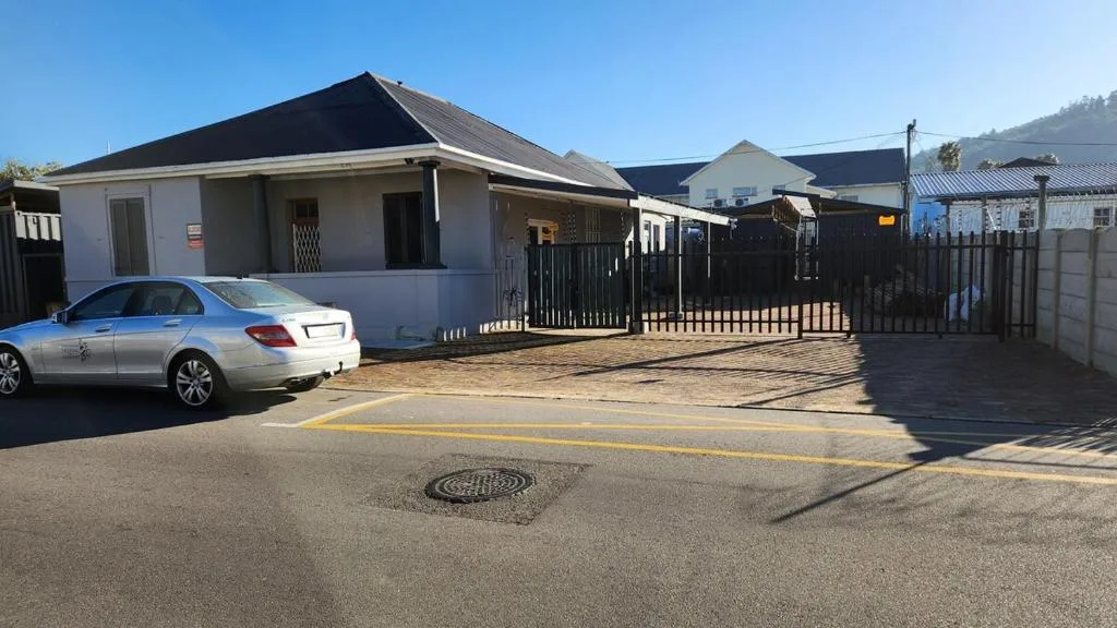 Modern single-story home with black roof, gated entrance, and parked silver car