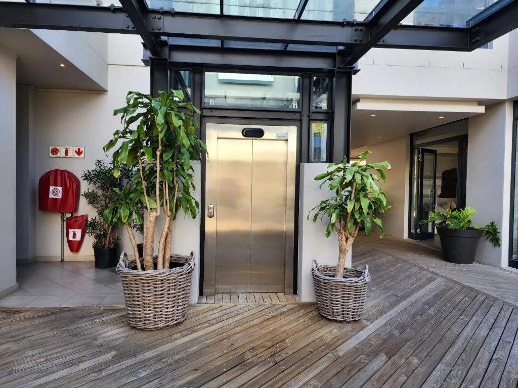 Modern covered deck with wooden flooring, potted plants, and elevator entrance