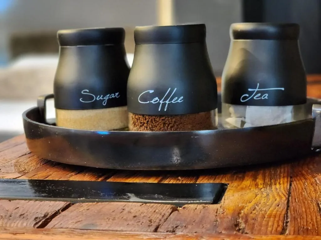 Three labeled black canisters for sugar, coffee, and tea on wooden surface