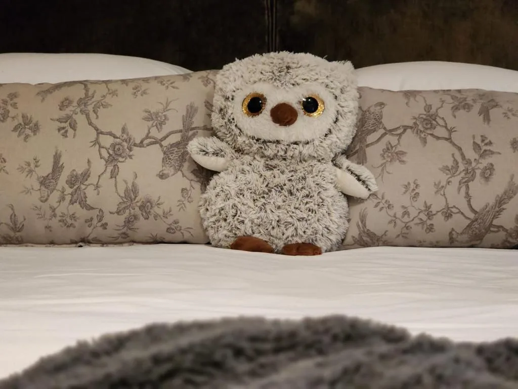 Cute stuffed owl toy sitting on bed with decorative pillows