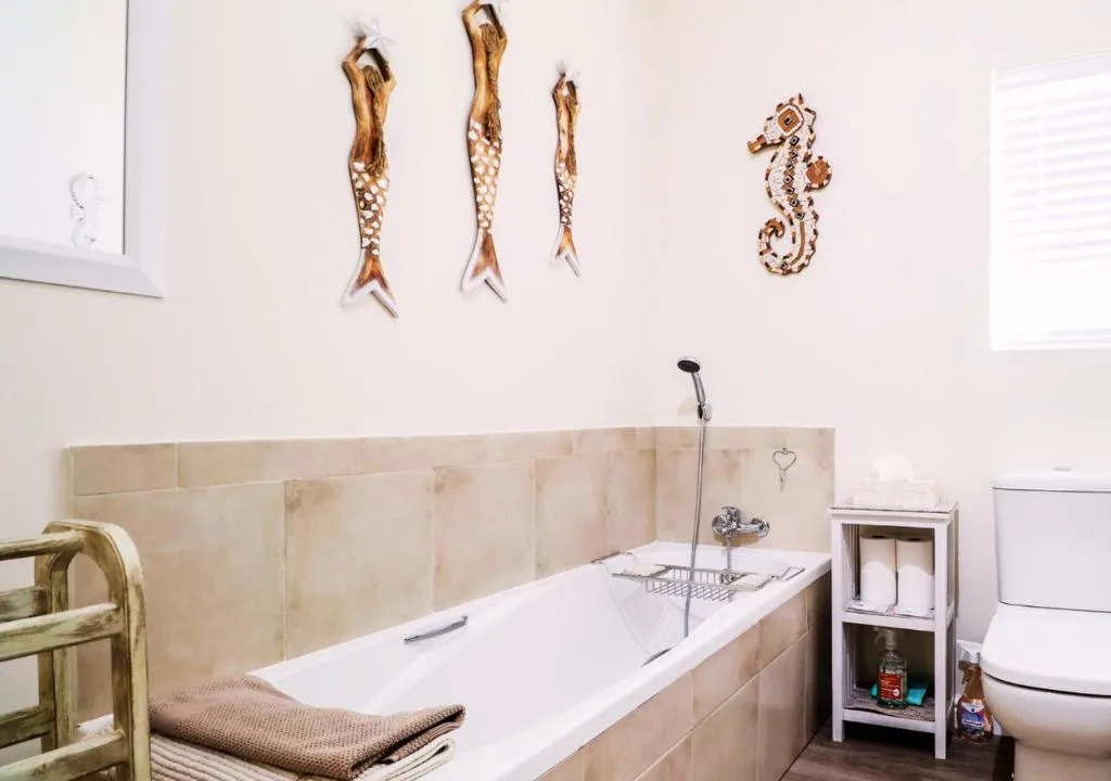 Beige tiled bathroom with bathtub, decorative sea creature wall art above