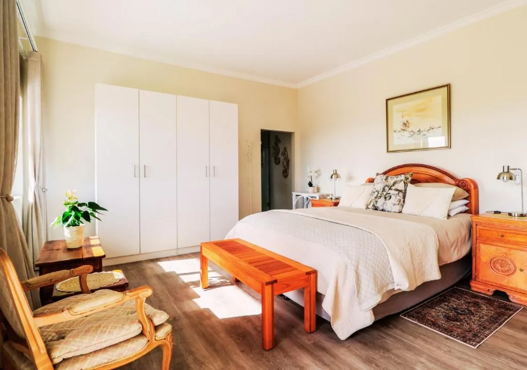 Bright bedroom with wooden bed frame, white wardrobes, and natural light