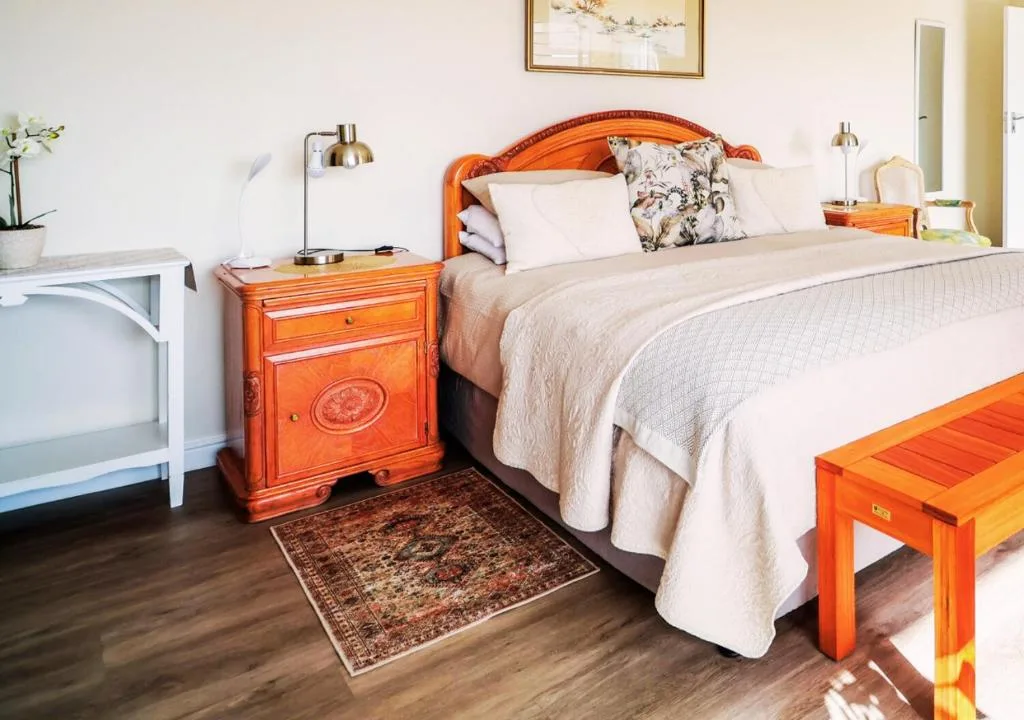 Bright bedroom with wooden bed frame, cream bedding, and orange nightstand