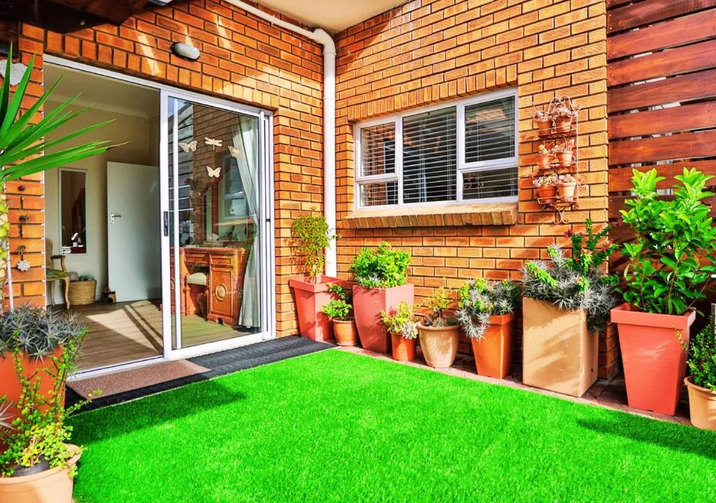 Brick courtyard with artificial lawn, potted plants, and patio seating area
