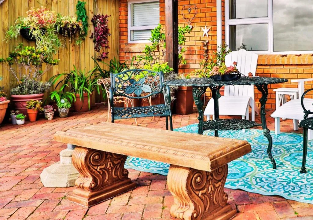 Brick patio with wooden bench, decorative seating, and potted plants