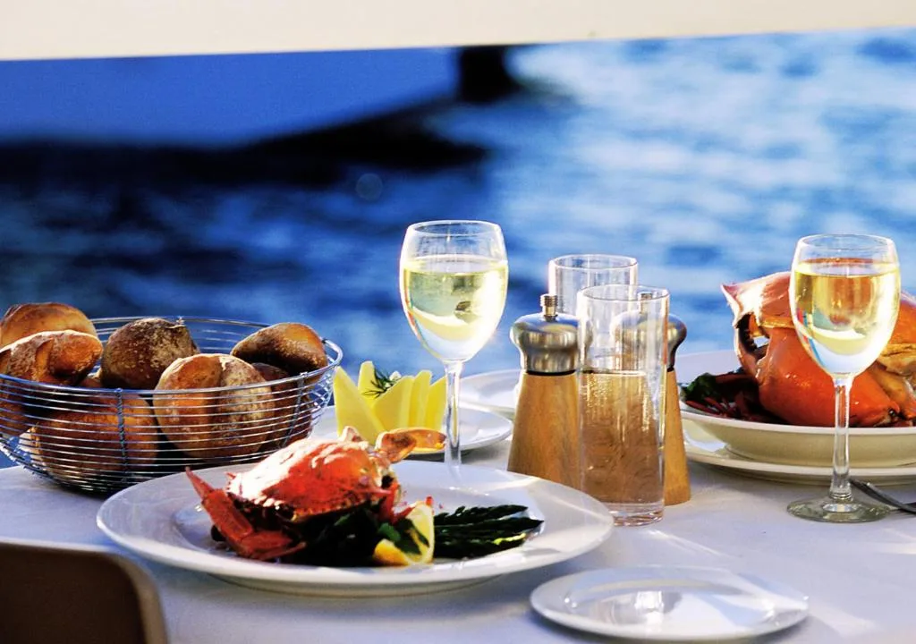 Waterfront dining setup with wine glasses and fresh seafood overlooking blue lagoon water