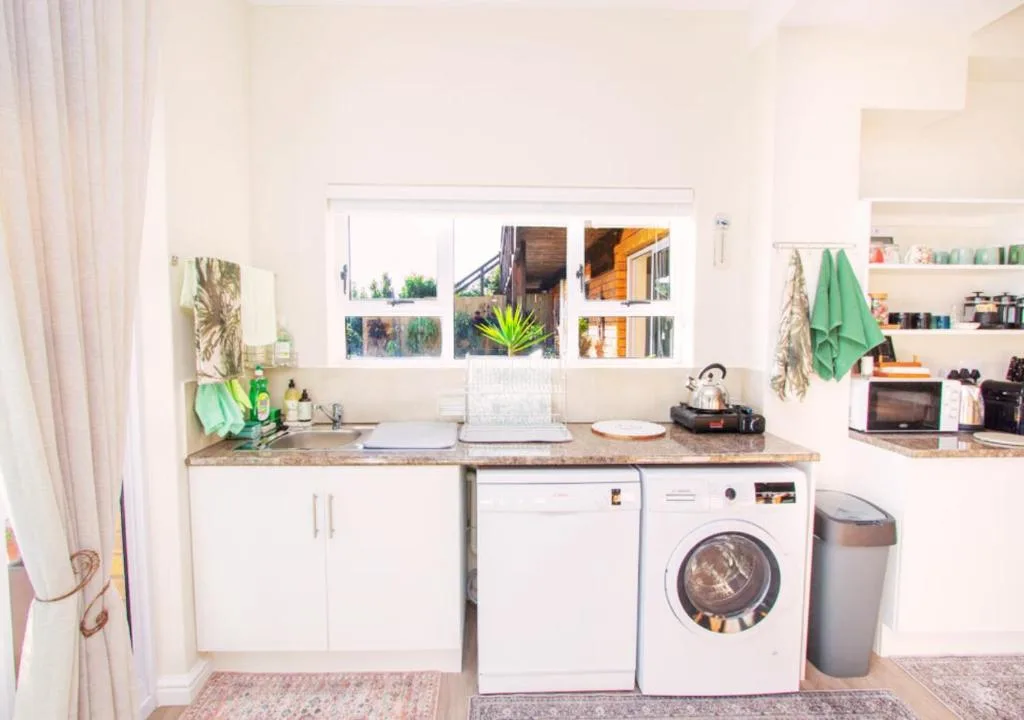 Modern kitchen with white cabinetry, granite countertop, washing machine, and appliances
