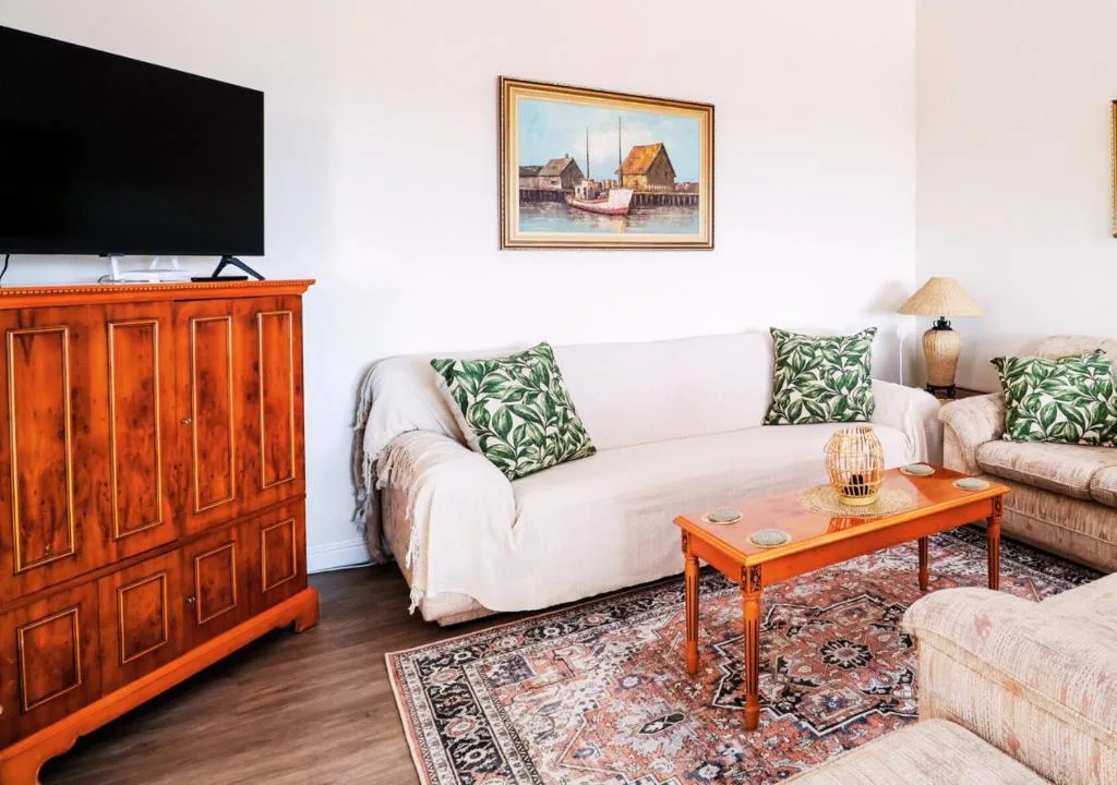 Bright lounge with cream sofas, orange wooden cabinet, patterned cushions and artwork