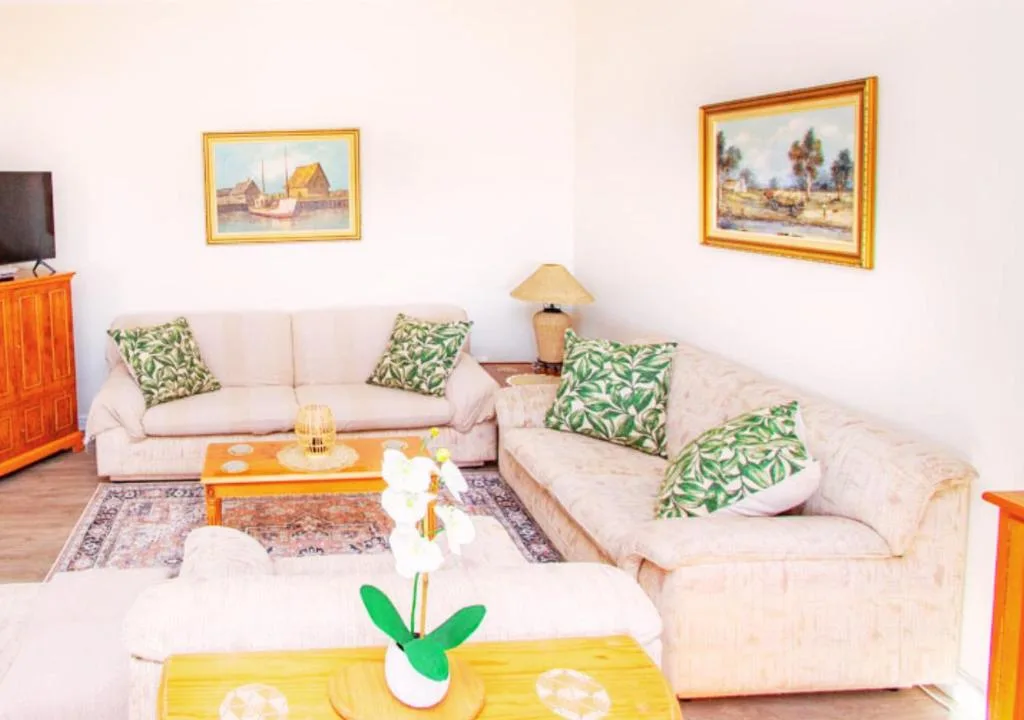 Spacious lounge with cream sofas, green patterned cushions, and framed artwork