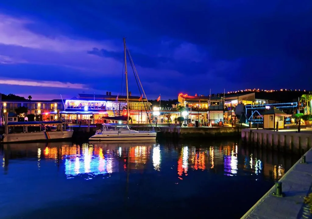 Knysna waterfront at dusk with illuminated shops and sailboat