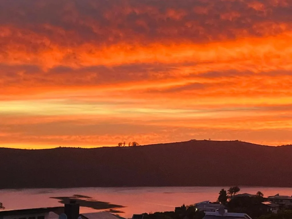 Dramatic orange sunset over Knysna Lagoon with forested hills silhouetted