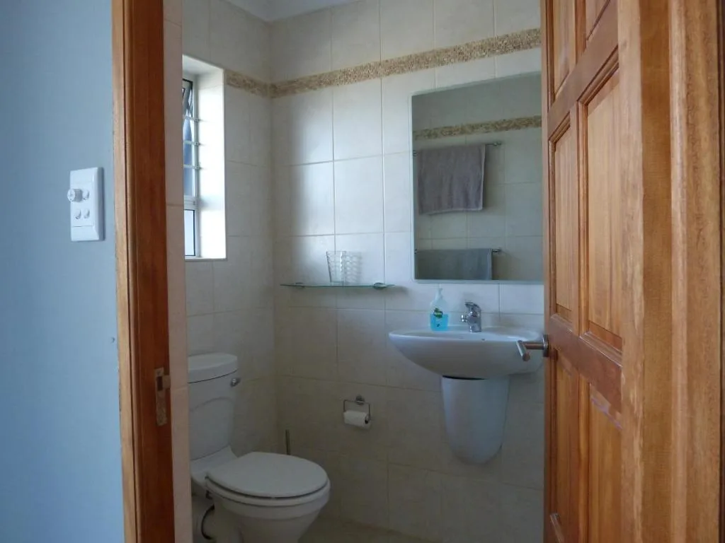 Clean bathroom with toilet, pedestal sink, mirror, and tiled walls