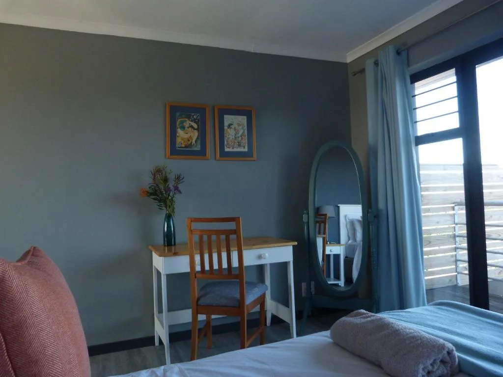Bedroom with desk, chair, bed, and ocean view through glass doors