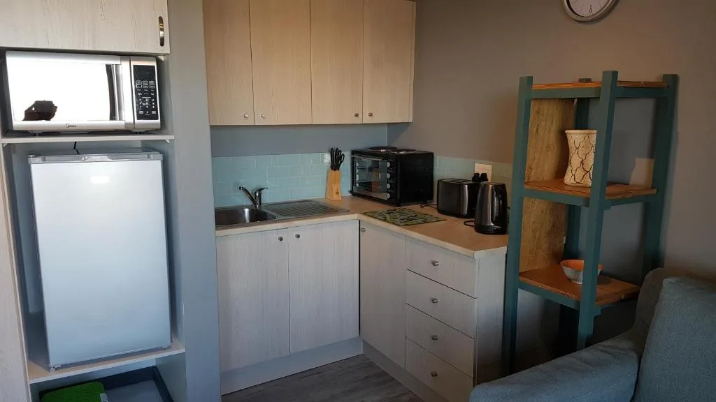 Compact kitchen with white cabinetry, microwave, toaster oven, and refrigerator