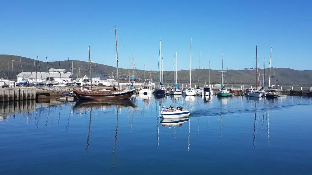 Calm harbor with sailboats and mountains reflected in blue water