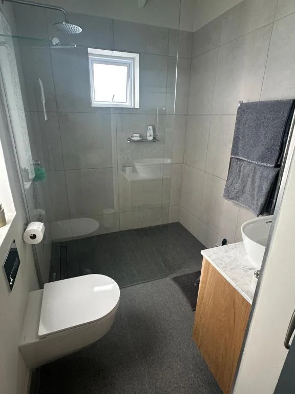 Modern bathroom with walk-in shower, toilet, vanity sink, and window