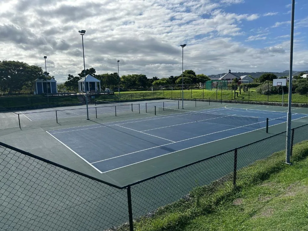 Multiple tennis courts with lighting poles and rural landscape surroundings