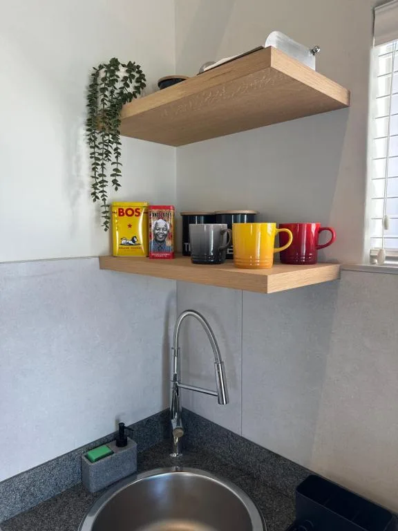 Modern kitchen corner with floating shelves, sink, and colorful mugs