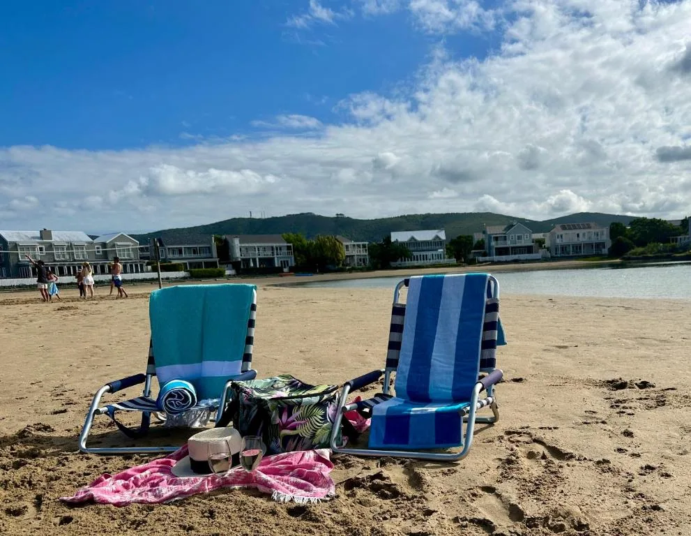Beach chairs facing sandy shore with waterfront properties and green hills beyond