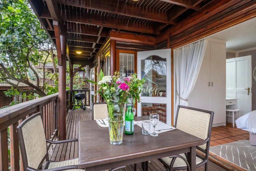 Covered wooden deck with dining table, chairs, and flowering centerpiece overlooking garden