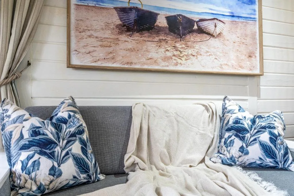 Coastal-themed lounge with gray sofa, blue patterned pillows, beached boats artwork