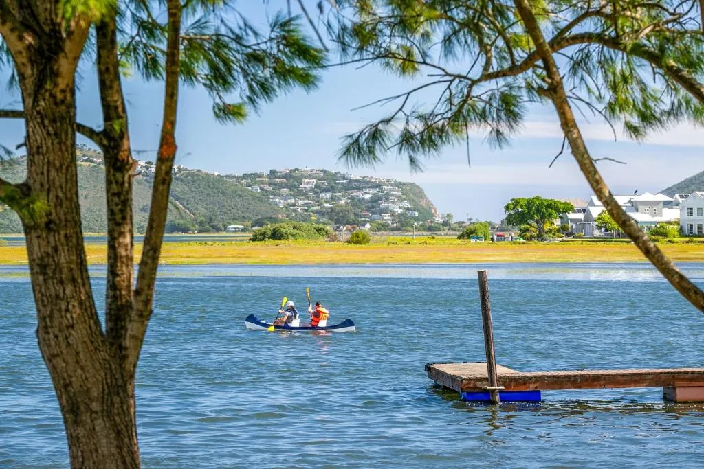 Scenic lagoon view with kayakers, mountains, and waterfront homes beyond