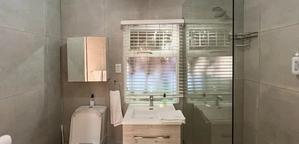 Modern bathroom with vanity sink, toilet, shower enclosure and window blinds
