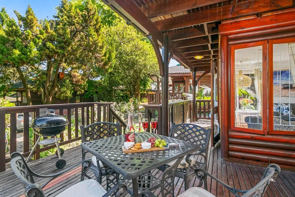 Covered wooden deck with dining table, braai grill, and lush garden views