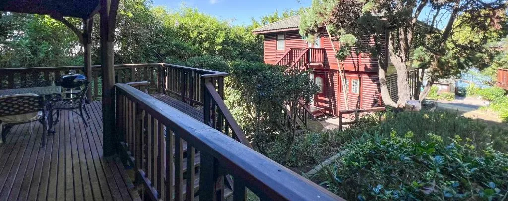 Wooden deck with black railings overlooking garden and red cottage