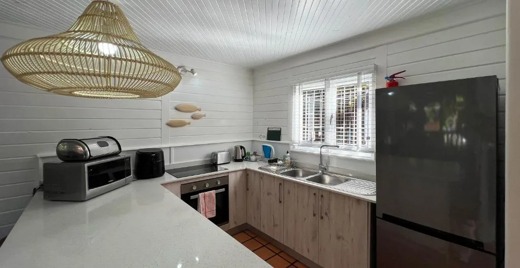 Modern kitchen with white cabinetry, stainless steel sink, black appliances and woven pendant light