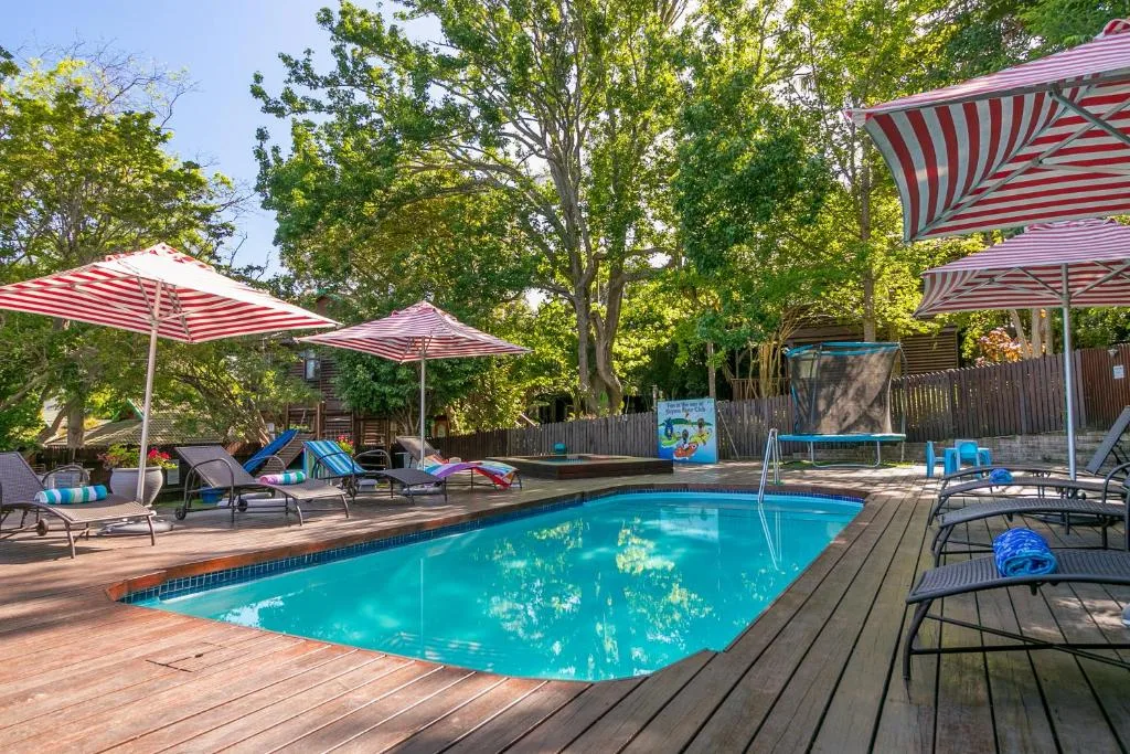 Sparkling swimming pool with wooden deck, red-striped umbrellas, and loungers
