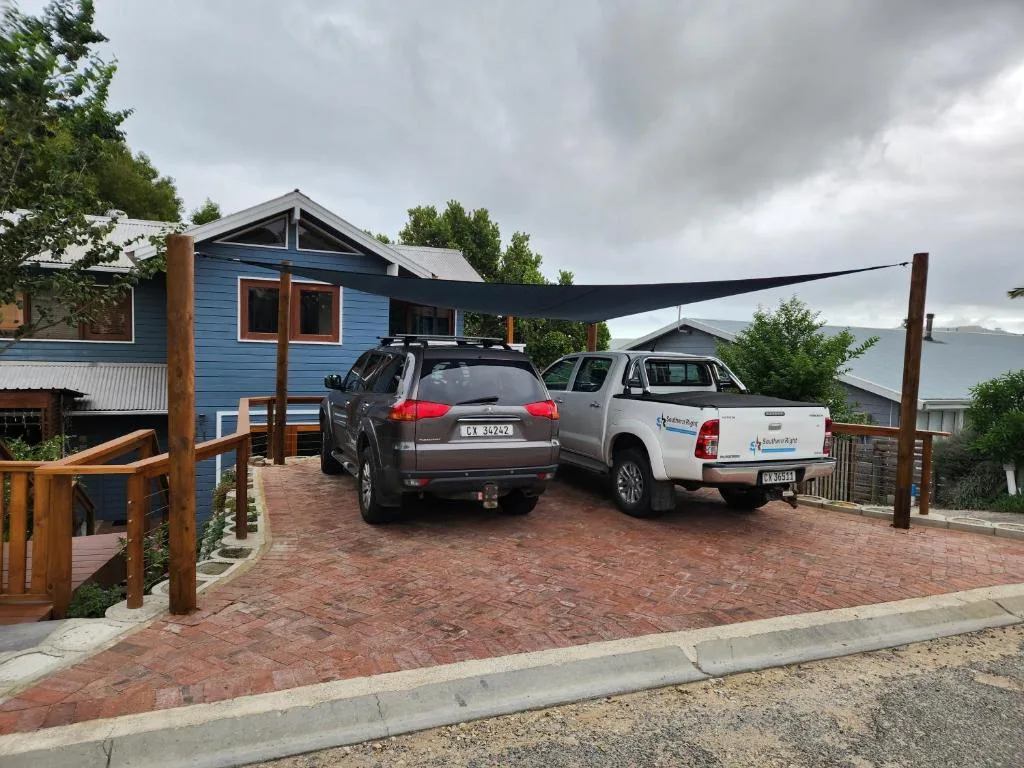 Blue cottage with brick driveway, parked vehicles, and mountain views beyond