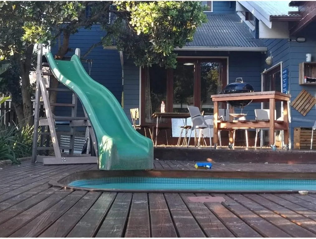 Swimming pool with green slide and wooden deck, facing house