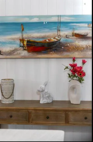 Decorative shelf with coastal artwork, flowers, and white decor pieces