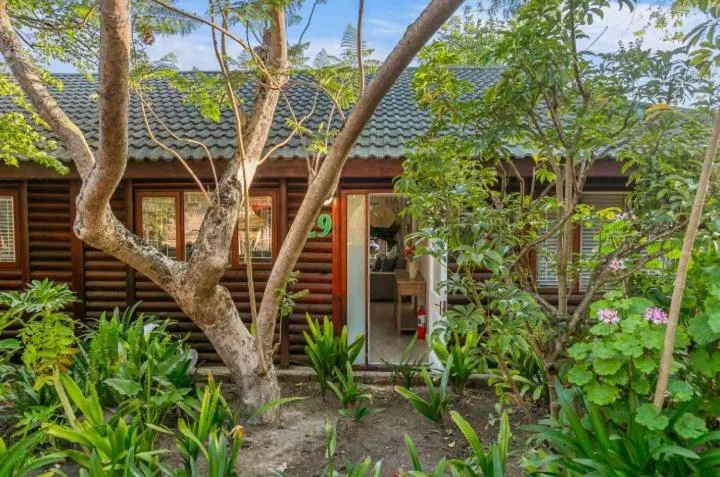 Log cabin exterior with mature trees and lush garden landscaping surrounding entrance
