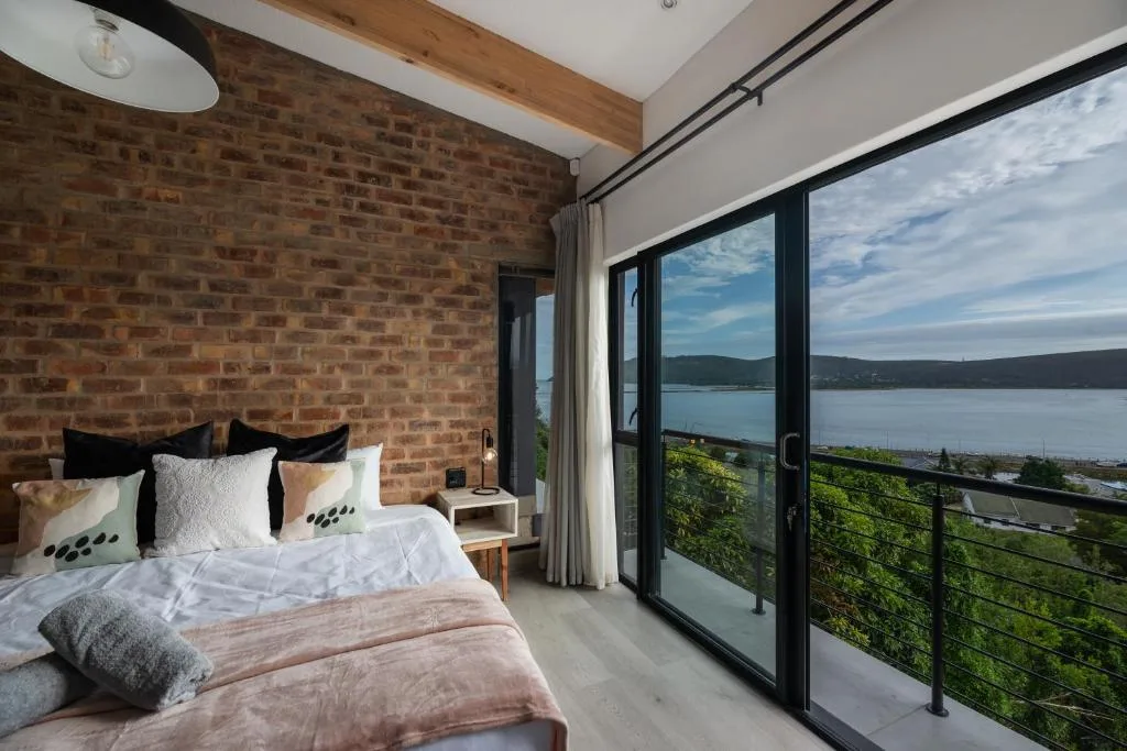 Modern bedroom with brick accent wall and lagoon views through glass doors