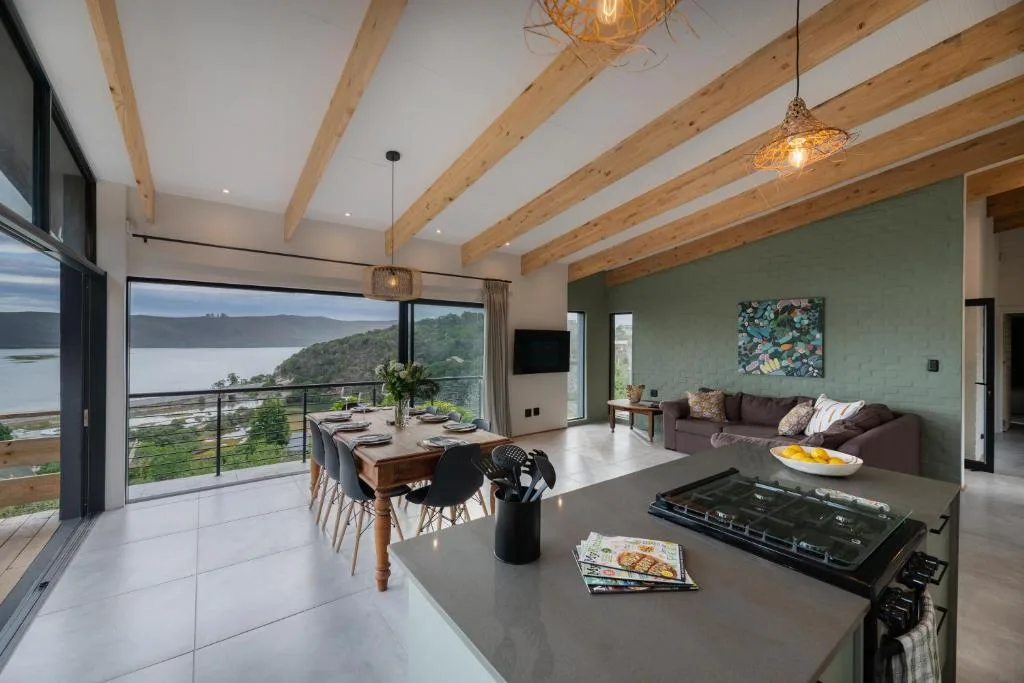 Modern living room with exposed beams, sofa, and panoramic lagoon views through glass doors
