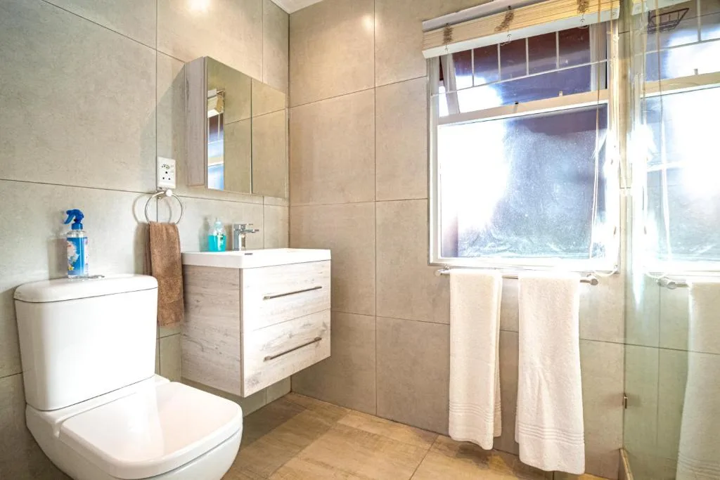 Modern bathroom with toilet, vanity sink, mirror, and shower area with window
